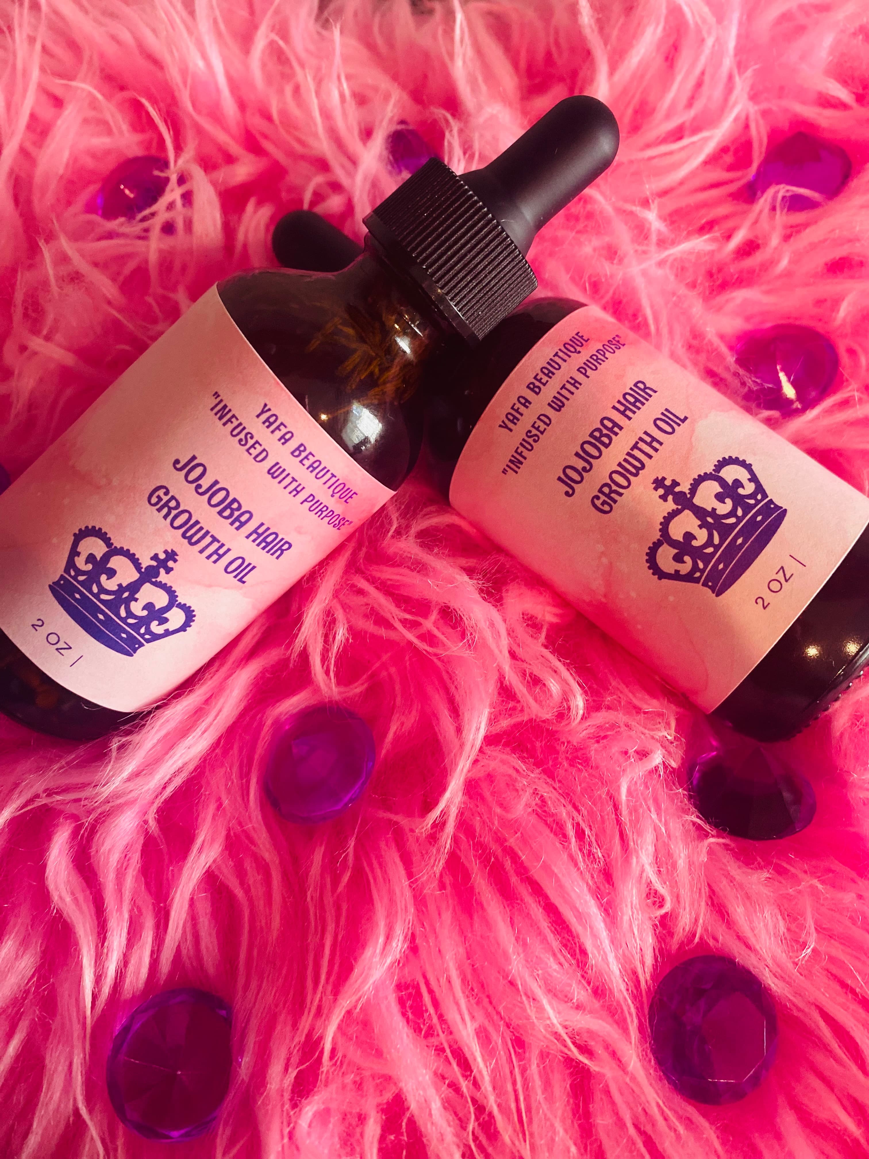Two bottles of jojoba hair growth oil on bright pink fur with purple faceted gems.